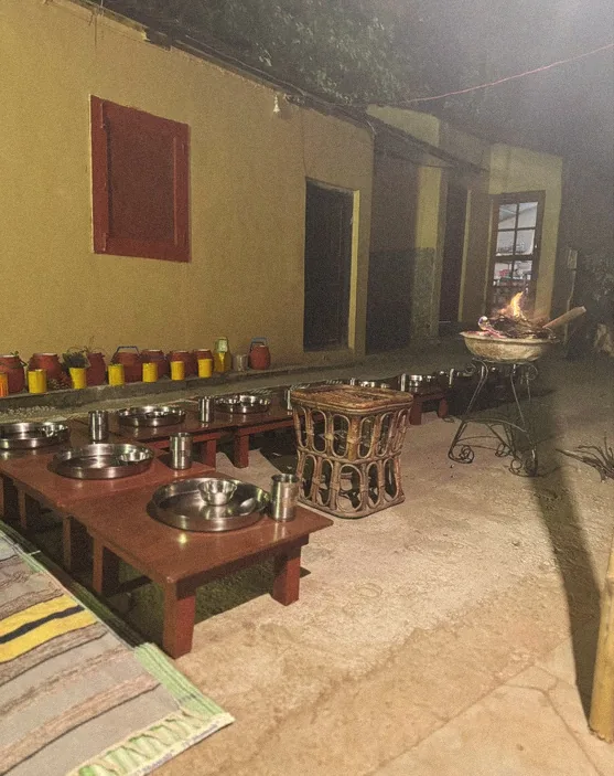 The Maatre chulha at night, low wooden tables and steel plates set around the clay stove