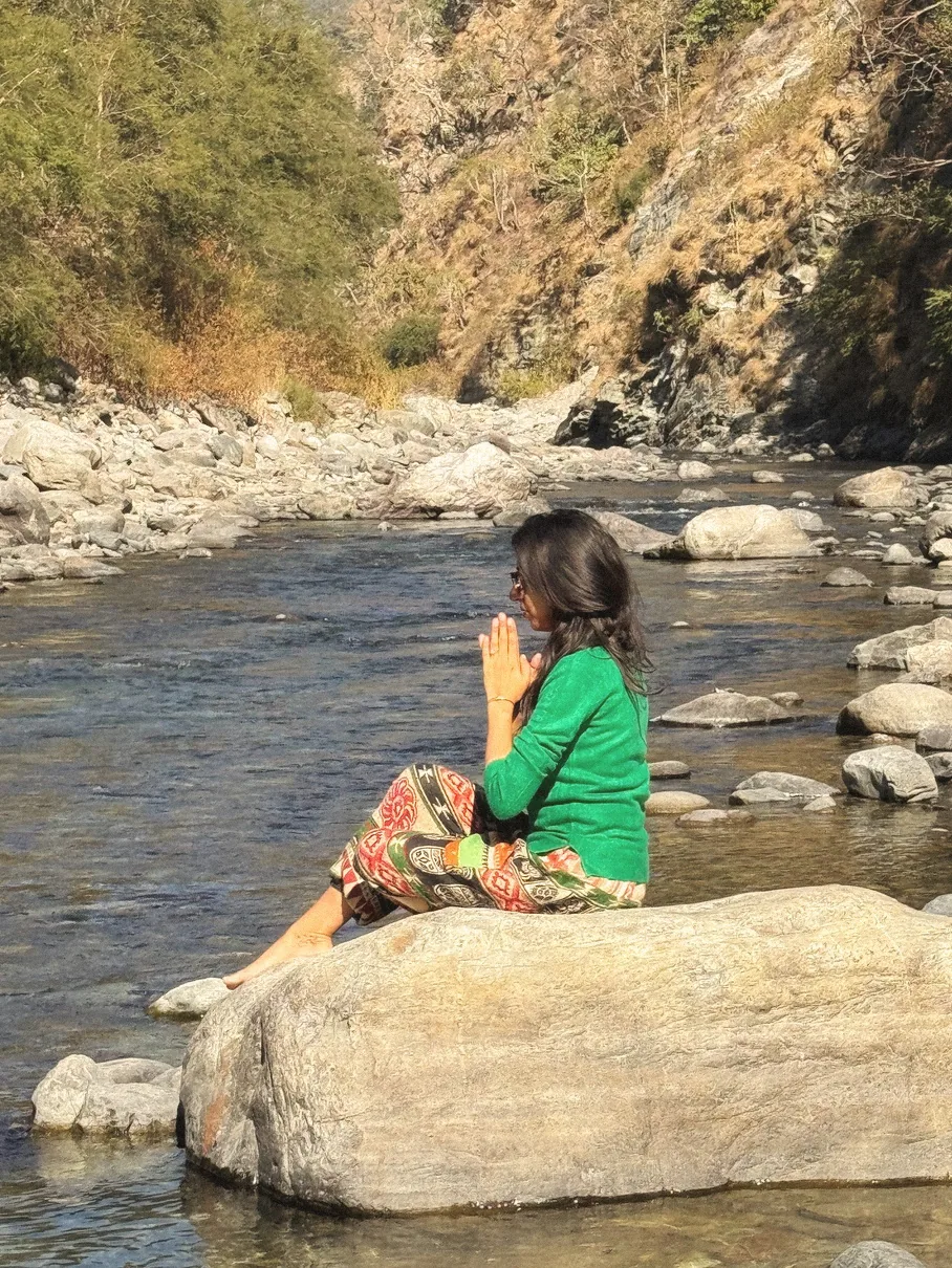 Heena sitting on a river rock with hands in prayer