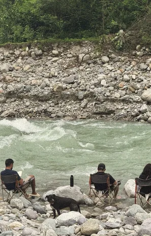 Guests sitting on camp chairs beside the Ramganga rapids