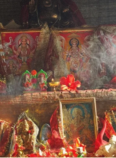 Home shrine with deity pictures, hibiscus and incense smoke