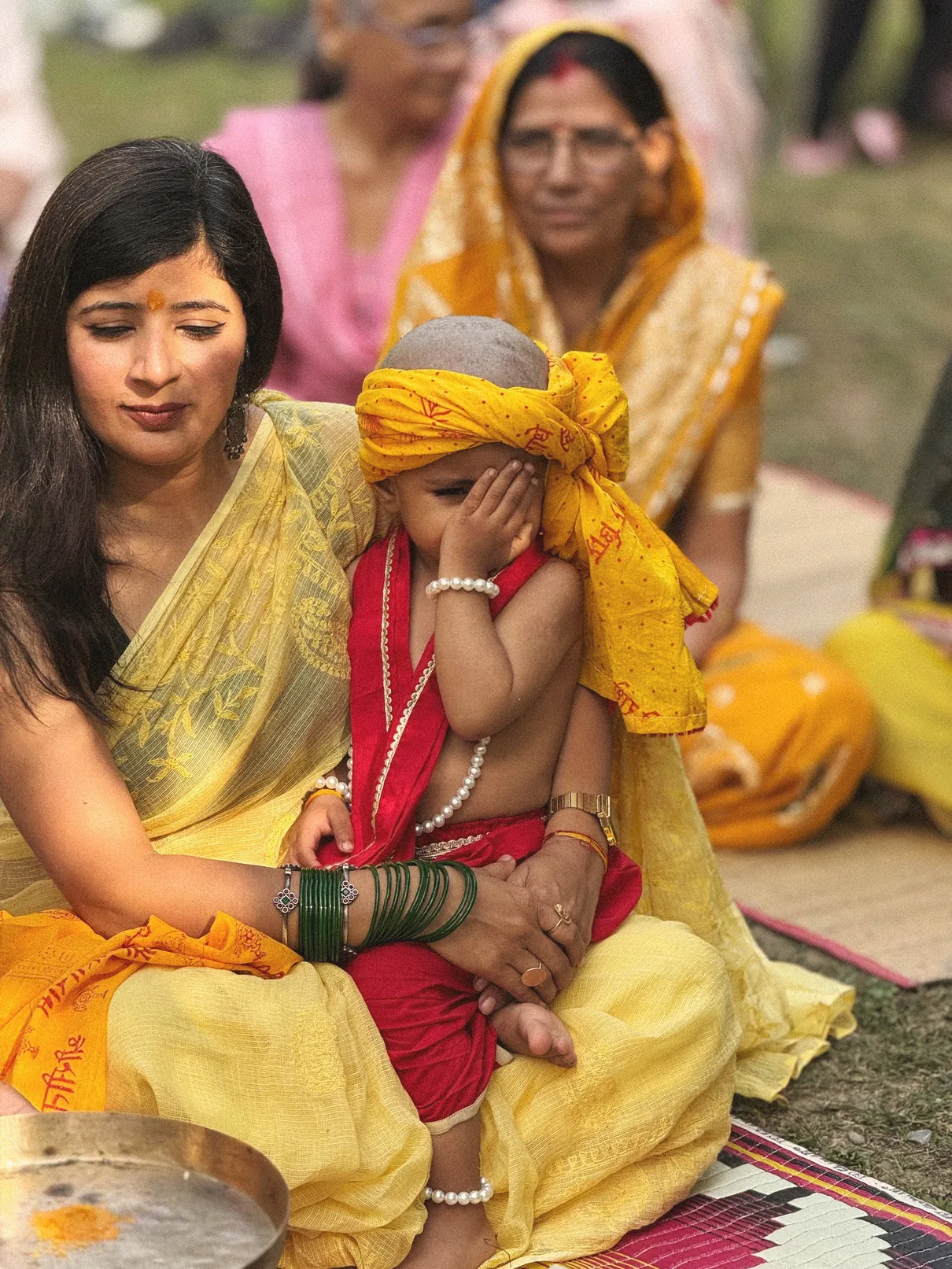 Mother holding her child in a saffron turban during the Chudakarna sanskar